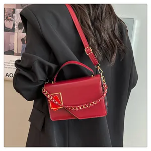 Sac bandoulière rouge avec rabat asymétrique et chaîne tressée porté par un mannequin
