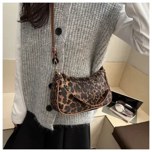 Detail view of the leopard print crescent bag featuring gold metal chain and leather strap
