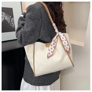 Detail of a large cream tote bag with brown trim and polka dot scarf detail on model