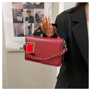 Détail du sac à main en cuir verni rouge avec boucle dorée et bandoulière en chaîne