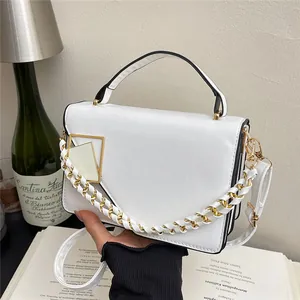 Sac à bandoulière blanc avec rabat asymétrique et chaîne dorée sur fond décoratif