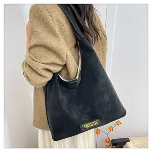 Detail of a large black matte hobo bag worn by a model in a brown blazer and white skirt