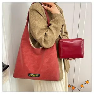 Macro detail of red matte leather tote bag featuring a brand logo tag and accessory pouch