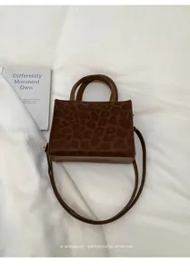 Detailansicht einer Handtasche mit Leopardenmuster und Lederbesatz auf weißem Stoff