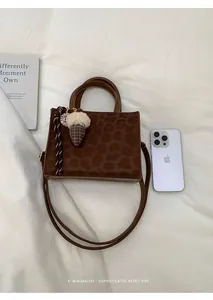 Flachbild einer kleinen Handtasche mit Leopardenmuster und Eichelanhänger auf weißem Stoff