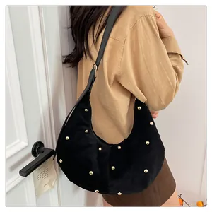 Detalle del bolso de media luna en terciopelo negro con remaches dorados y correa