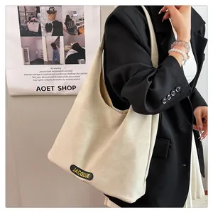 Close-up of the beige leather tote bag featuring a black oval logo and wide shoulder strap