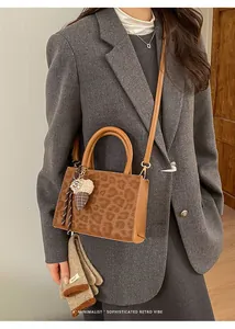 Detail der Handtasche mit Leopardenmuster, braunen Griffen und Zierschleife auf grauem Anzug