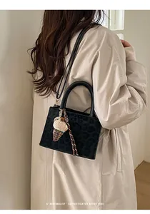 Details der schwarzen Umhängetasche mit Leopardenmuster und Eiscreme-Anhänger am Trenchcoat