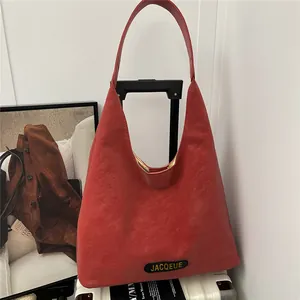 Chic red tote bag with wide shoulder strap hanging on a white suitcase handle