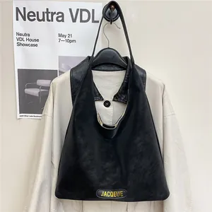 Elegant black faux leather tote bag with gold logo shown in a stylish minimalist setting