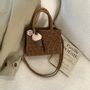 Schicke Handtasche mit Leopardenmuster, Eiscreme-Anhänger und Schultergurt auf weißem Stoff