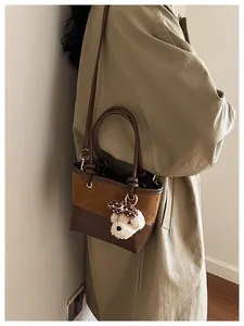Detail der Wildleder-Eimertasche mit braunem Patchwork-Design und Teddybär-Anhänger