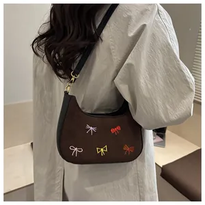 Sac sous le bras en daim marron avec broderies de nœuds colorés porté par un mannequin élégant