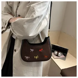 Sac demi-lune en daim marron avec broderies de nœuds colorés porté à l'épaule