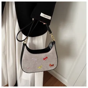 Détail de broderies nœuds colorés sur sac gris avec finitions en cuir noir élégant