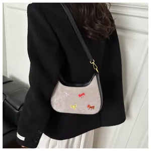 Détail des broderies de nœuds colorés et ferrures dorées sur le sac baguette en denim