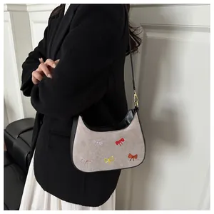 Détail de nœuds colorés brodés sur un sac en daim gris avec bandoulière en cuir noir
