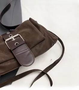 Detail of soft brown suede baguette bag featuring a wide strap and silver metal buckle