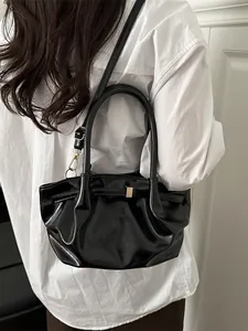 Sac panier de luxe français en cuir verni noir avec boucle dorée porté par un mannequin