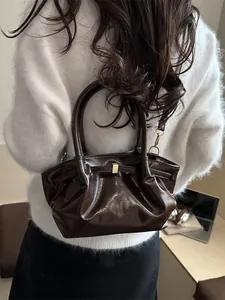 Sac à main chic en cuir marron foncé brillant avec boucle dorée sur pull en maille blanc