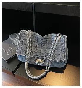Detalle de bolso de mezclilla acolchada azul con cadena plateada y cierre de giro