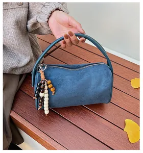 Blue suede cylinder pillow bag with wooden bead charm detail held by model