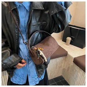 Close-up of brown suede cylindrical pillow bag featuring wood bead tassel and leather strap