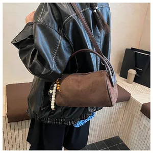 Detail of vintage brown suede cylinder bag with beaded charm and dark leather handles