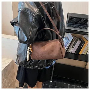 Close-up of coffee brown suede cylindrical bag with decorative beaded keychain tassel