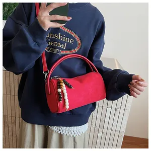 Detail view of red frosted suede cylinder bag with beaded charm and shoulder strap