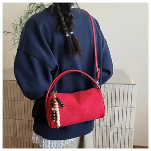 Detail of red vintage suede cylinder bag with beaded charm on shoulder strap