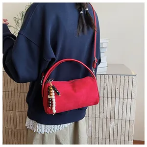 Detail view of red suede cylinder bag with beaded charm and arc-shaped handle