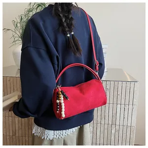 Detail of red suede cylinder bag with colorful beaded charm and smooth matte texture