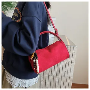 Detail of red suede cylinder bag featuring a colorful beaded tassel and smooth top handle