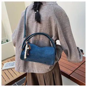 Detail of navy blue suede cylinder bag with vintage wooden bead charm on shoulder strap