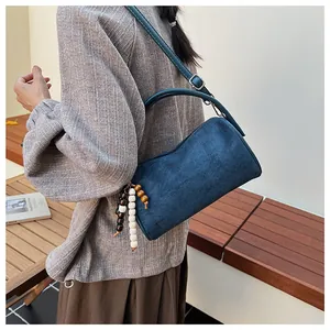 Detail of dark blue suede shoulder bag with rustic wooden bead charm and long leather strap