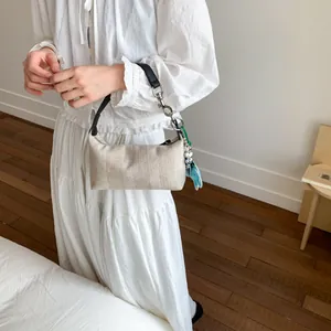 Minimalist beige canvas dumpling bag with black handle and decorative charm in bright room