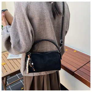 Close-up of black matte suede boston bag with wooden bead charm and silver hardware details