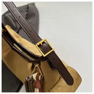 Détail du sac bandoulière en daim marron avec boucle dorée et breloque pompon tressé