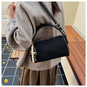 Close-up of black suede underarm bag with wooden bead charm in an outdoor setting