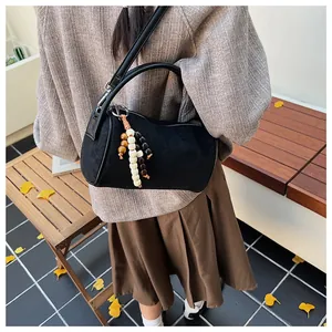 Detail of black suede cylinder bag with colorful beaded tassel and leather strap