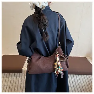 Détail du sac hobo en daim marron foncé avec pompon perlé porté sur un trench-coat