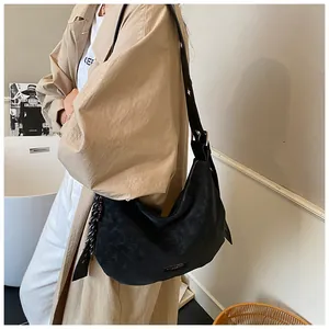 Détail du sac hobo en daim noir avec plaque logo métallique et pompons décoratifs