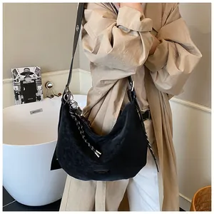 Détail du sac demi-lune en daim noir avec bandoulière tissée dans un décor minimaliste