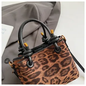 Close-up of leopard print suede handbag featuring black leather handles and gold metal accents