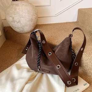 Sac hobo rétro en daim marron foncé avec de grands œillets métalliques et un pompon