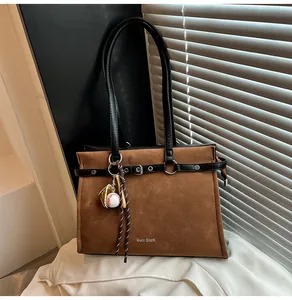 Detail of brown suede tote bag featuring a decorative black strap and metal buckle