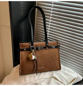Detail of brown suede tote bag with black leather straps and baseball charm accessory