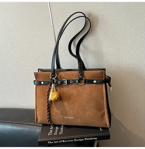 Detail of a large brown suede tote bag with black leather trim and baseball bat charm